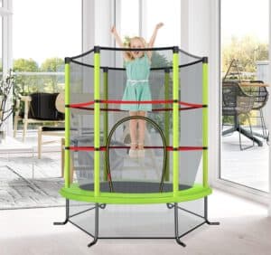 Mädchen springt freudig auf einem grünen Kindertrampolin mit Sicherheitsnetz in einem modernen Wohnzimmer